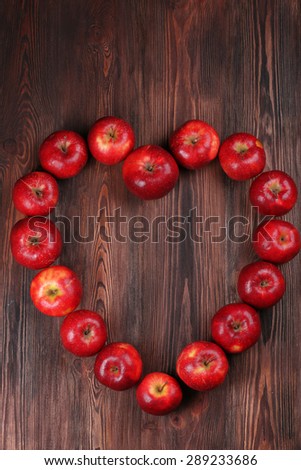 Ripe red apples in shape of heart on wooden background