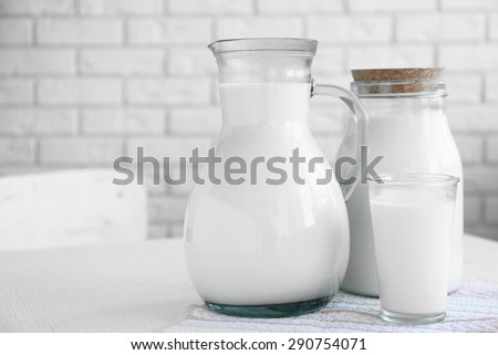Pitcher, jar and glass of milk on wooden table, on bricks wall background