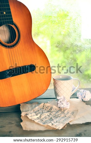 Acoustic guitar and cup of tea next the window with rain drops