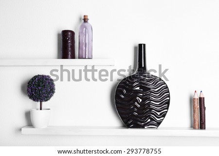 Decorative vases on wooden shelf  on white wallpaper background