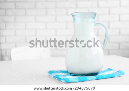 Pitcher of milk on wooden table, on bricks wall background