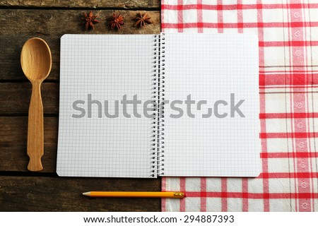 Open recipe book and spices on napkin, on wooden background