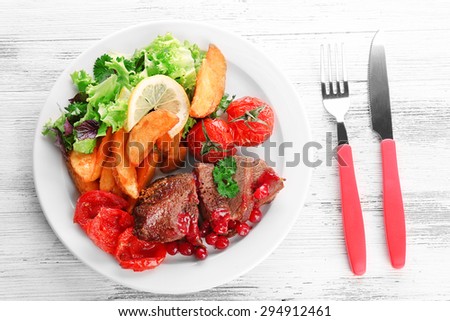 Tasty roasted meat with cranberry sauce and roasted vegetables on plate, on color wooden background