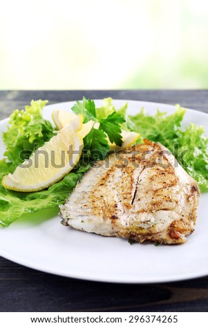 Dish of fish fillet with greens and lemon on bright background