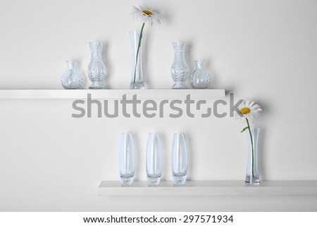 Decorative glass vases with flowers  on wooden shelf  on white wallpaper background