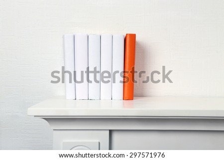Blank books and orange one on shelf on white wallpaper background