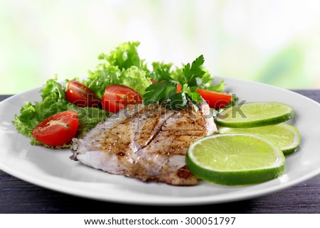 Dish of fish fillet with salad and lime on bright background