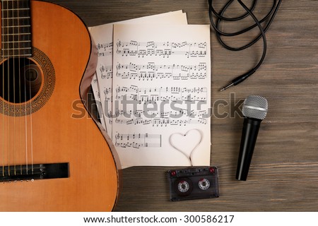 Music recording scene with classical guitar, music sheets, cassette and microphone on wooden table, closeup