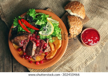 Tasty roasted meat with cranberry sauce, salad and roasted vegetables on plate, on wooden background