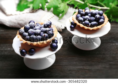 Delicious crispy tarts with black currants on white stand on wooden table, closeup