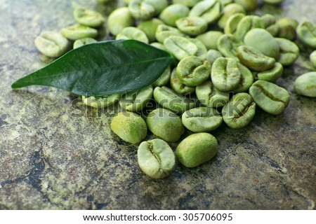 Heap of green coffee beans with leaf on table close up