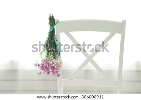 Bouquet of wild flowers drying on chair on light background