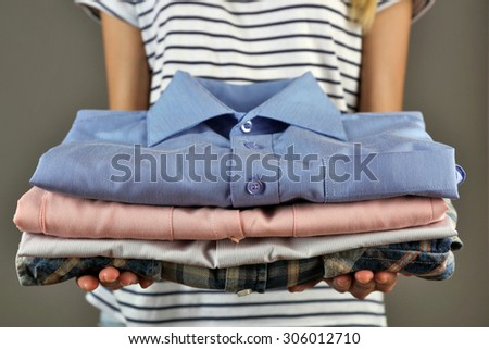 Woman holding shirts on gray background