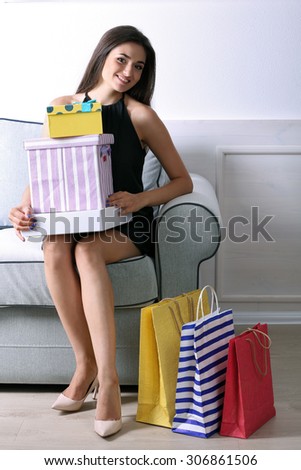 Beautiful young woman with shopping bags and boxes sitting on sofa in room