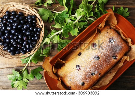 Freshly baked cake with black currants in brown pan on wooden table, top view