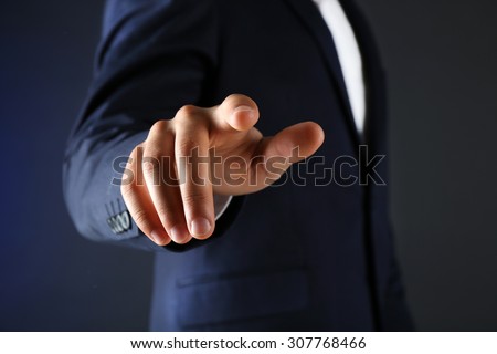 Businessman in suit points on something on dark background