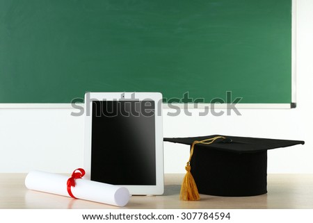 Graduation cap with tablet and diploma on table in class