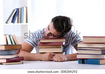 Young man sleeping with books at table in room