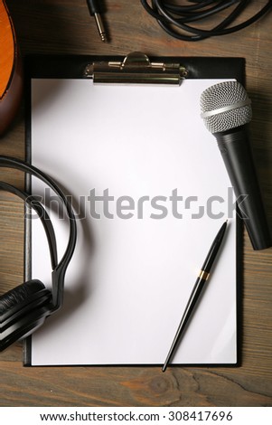 Music recording scene with classical guitar, headphones, microphone and memo pad on wooden table, closeup