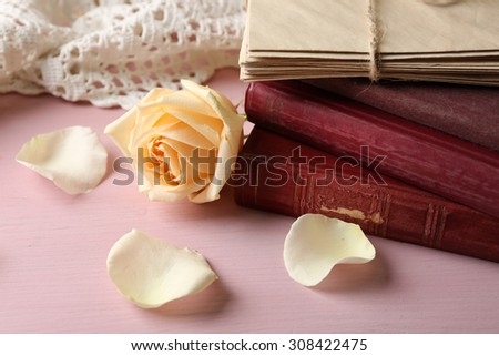 Fresh rose flower with old book and letters on color wooden table background. Vintage concept