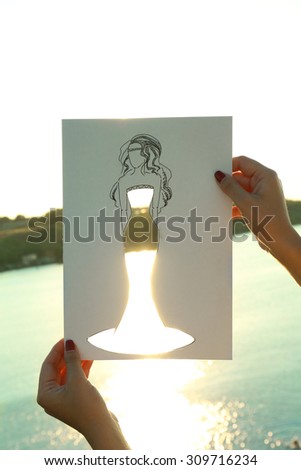 Drawing woman in cutout dress on sheet of paper on nature background
