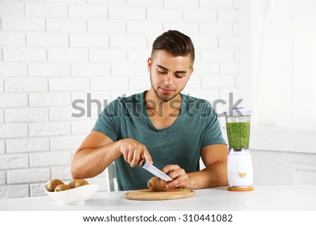 Young man cutting kiwi, preparing orange juice