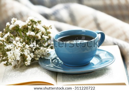 Blue cup of coffee with open book on sofa in room