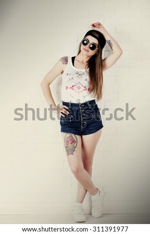 Beautiful girl with stylish make-up and tattooed body on light background