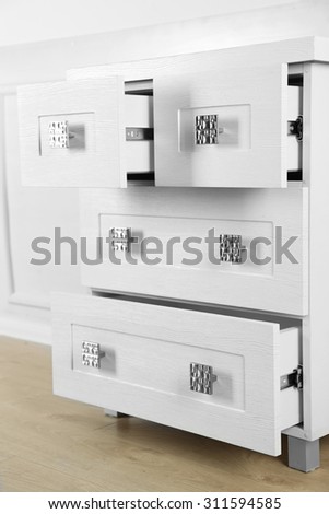 White wooden chest of drawer in the interior of an room.  Open drawers