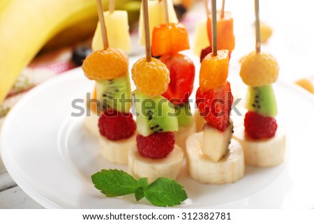 Fresh fruits on skewers in plate on table, closeup