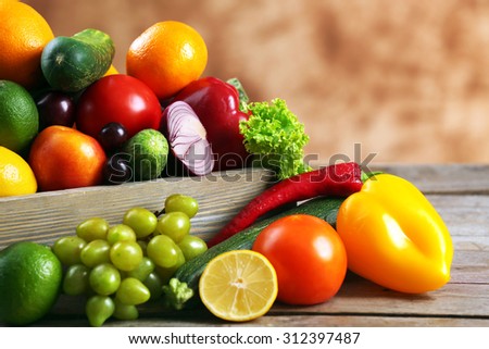 Heap of fresh fruits and vegetables in crate on wooden table close up