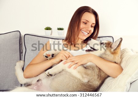 Woman sitting with her malamute dog on sofa in room