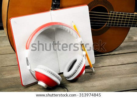 Music recording scene with classical guitar, memo pad and headphones on wooden table, closeup