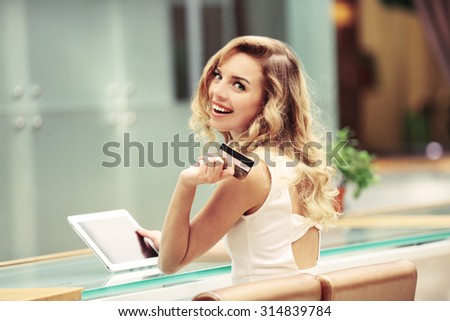 Beautiful young woman with digital tablet and credit card in cafe