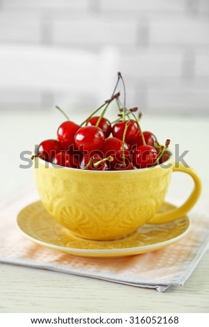 Cherries in mug on table, on light background