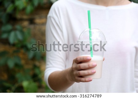 Woman holding plastic cup of milkshake  close-up, outdoors