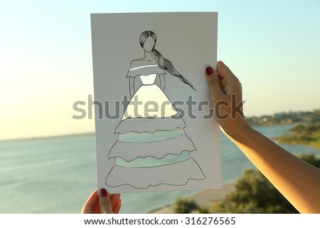 Drawing woman in cutout dress on sheet of paper on nature background