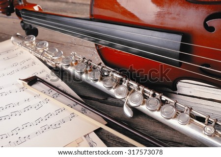 Flute and violin with music notes on wooden table close up