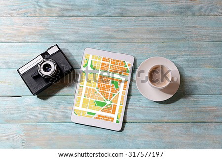 Tablet with map gps navigation application, camera and cup of coffee on wooden background