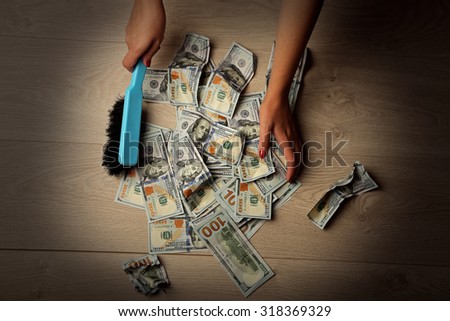 Woman broom sweeps dollars in heap on wooden floor background