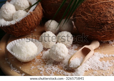 Candies in coconut flakes and fresh coconut on wooden board, close-up