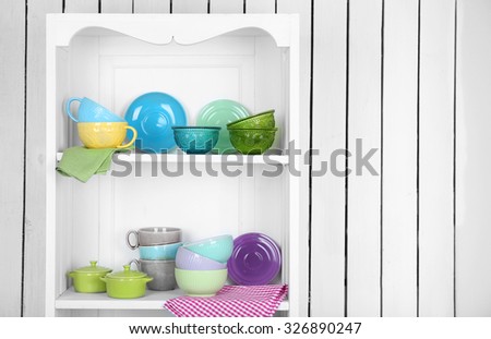 Clean glasses, plates and cutlery on shelves in kitchen cupboard