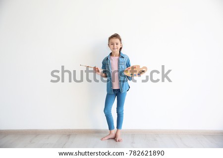 Little girl with watercolors and brush against white wall indoors