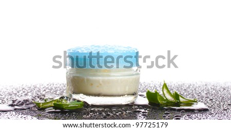 Closed glass jar of cream and aloe on black table with water droplets isolated on white
