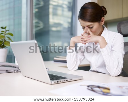 asian businesswoman sitting in office, looking tired.