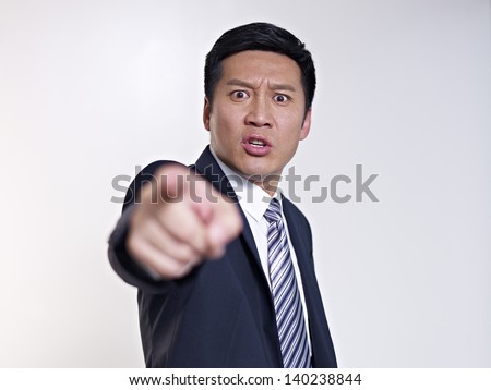 angry asian businessman pointing at camera, focus on face.