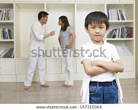 6-year old asian boy with quarreling parents in background.