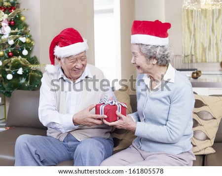 Asian senior couple with Christmas hats exchanging gifts.