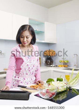 asian woman touching screen of tablet computer in kitchen.