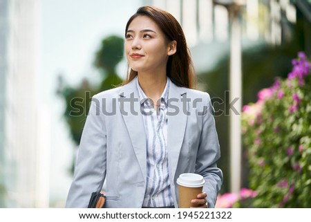 successful young asian female white collar office worker walking on street looking away holding cup of coffee